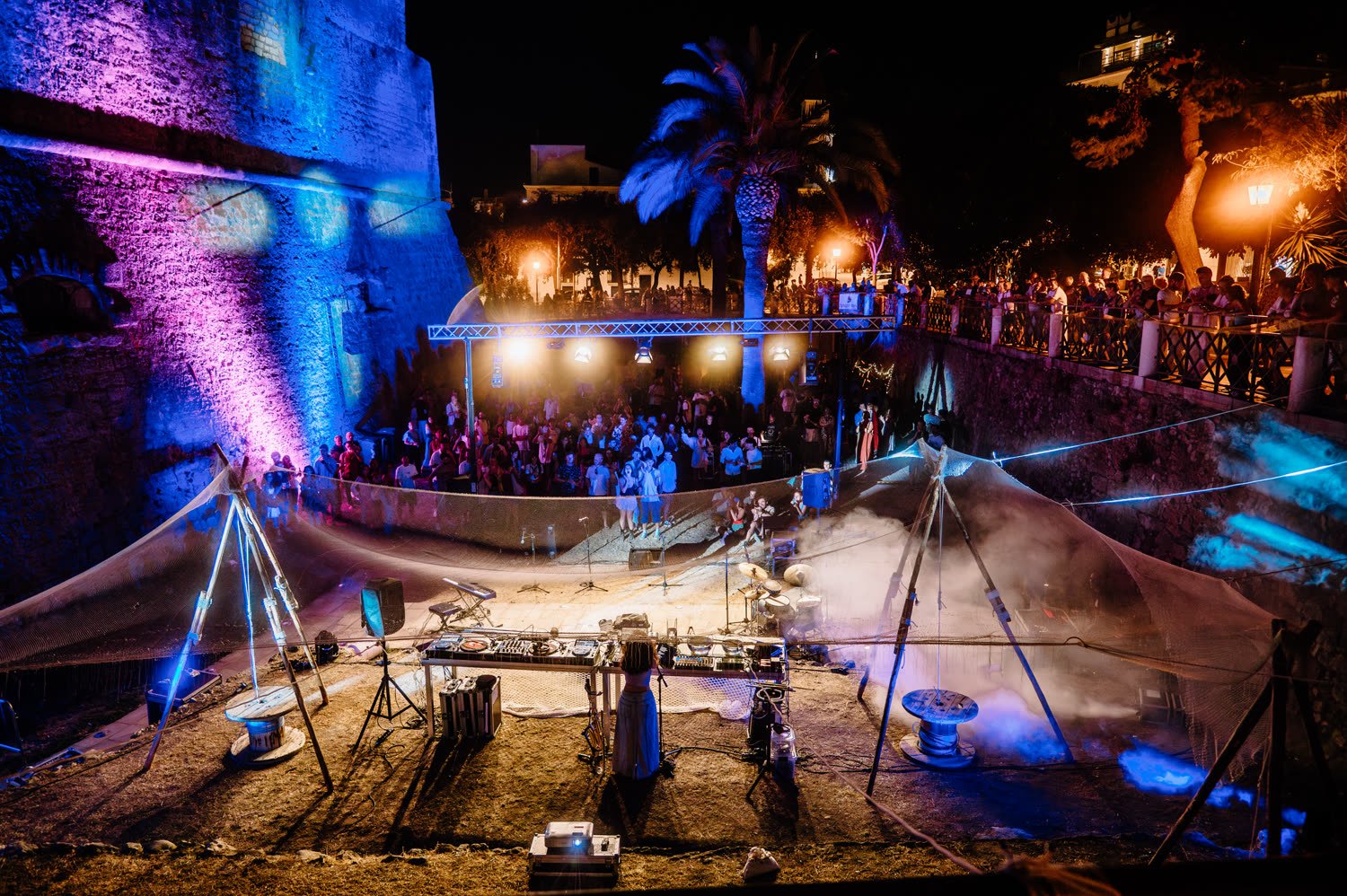 Wide shot of the courtyard at night, stage lit blue and pink